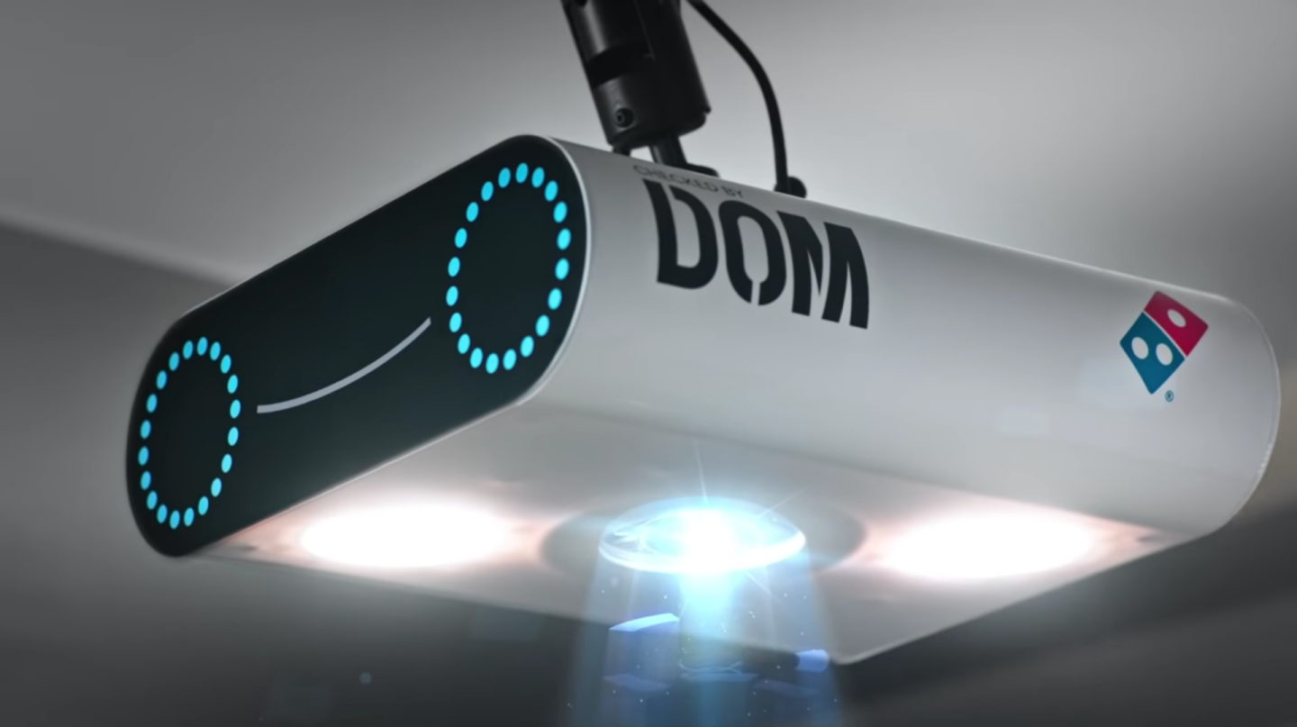 The technology is built into a scanning device called the DOM Pizza Checker, which sits above the cut bench to run a final inspection on Domino's pizza pies before they're handed over to the delivery person