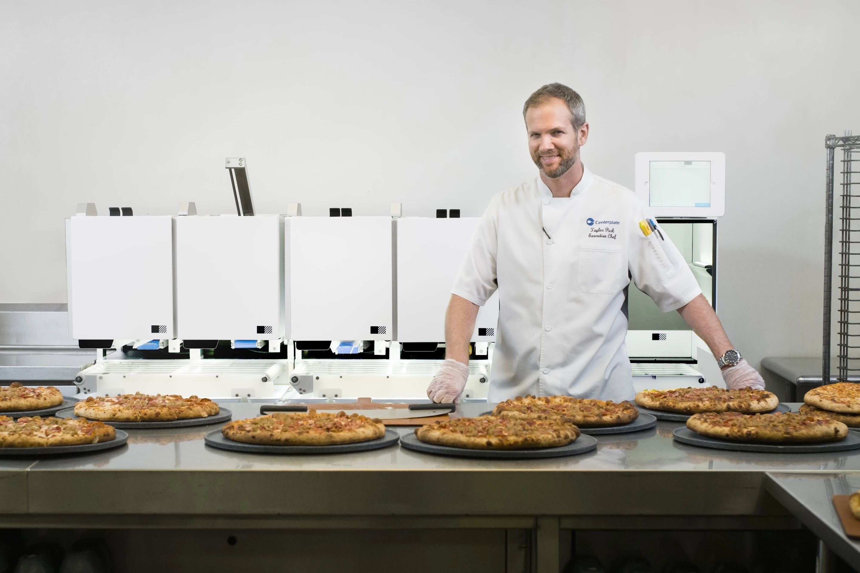 Centerplate Executive Chef Taylor Park stands in front of Picnic's automated pizza assembly robot at T-Mobile Park