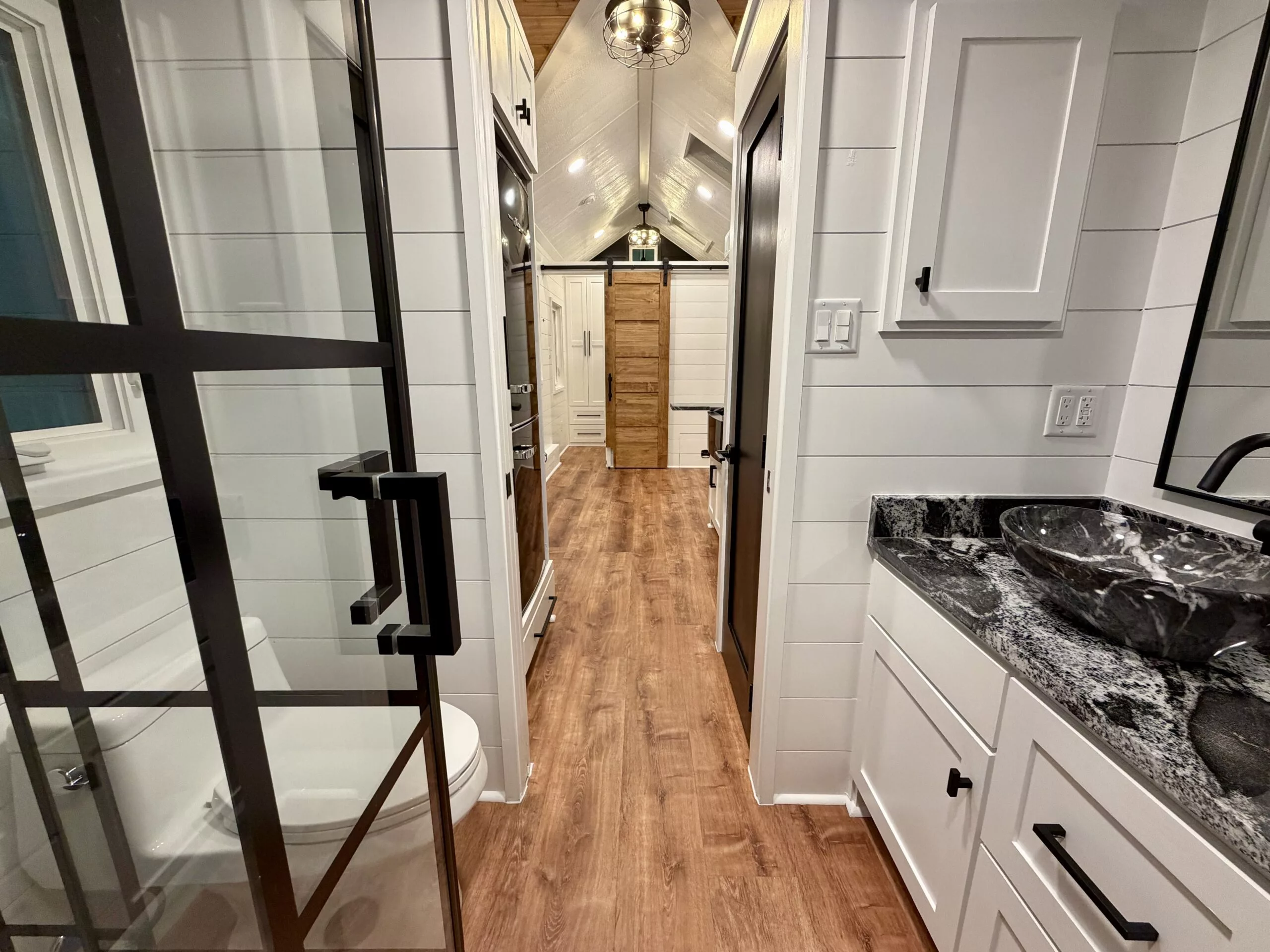 The Betty tiny house's bathroom includes a vanity sink, a glass-enclosed shower, a flushing toilet, and a stacked washing machine and dryer