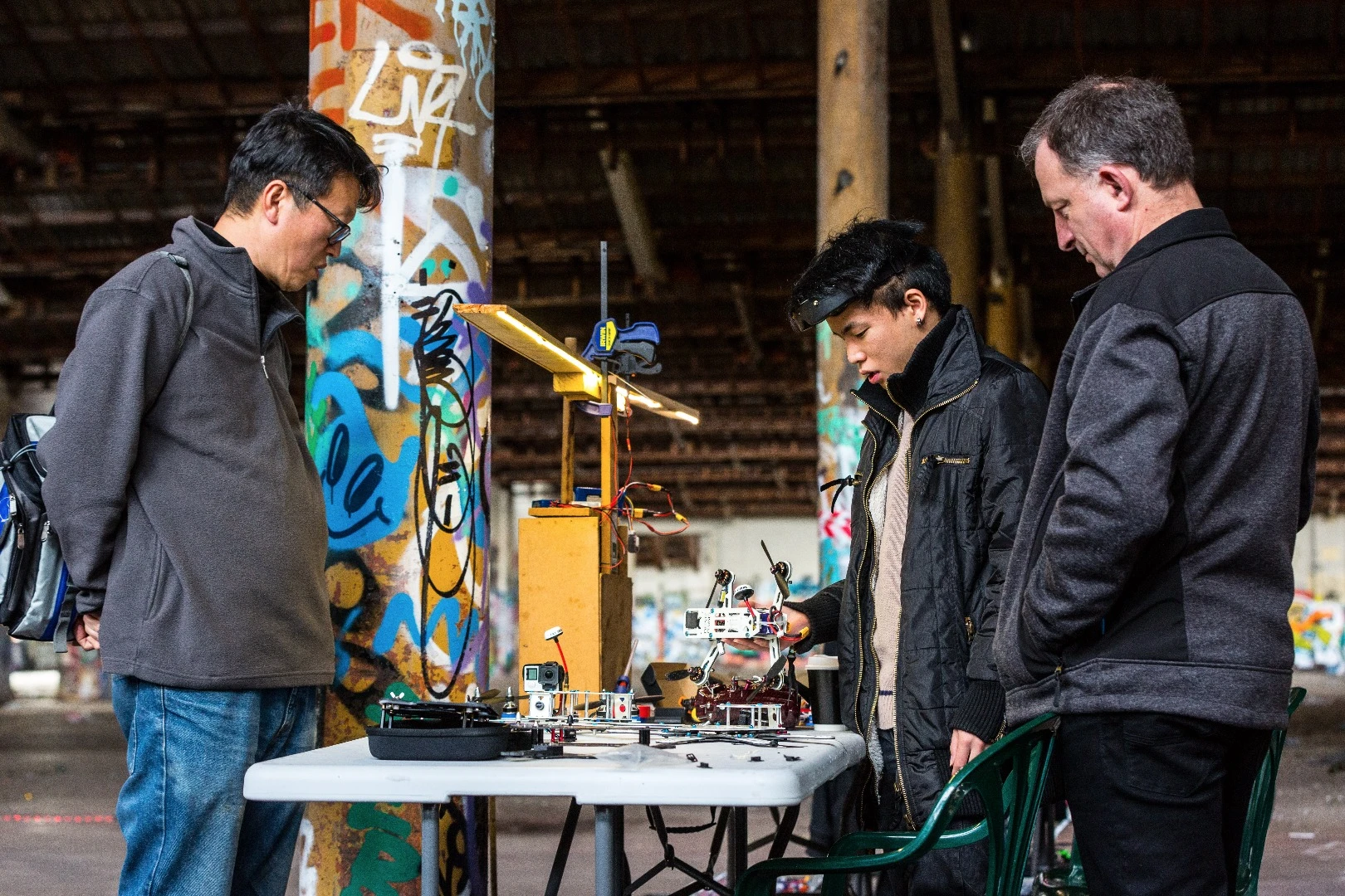 Onlookers lounge in camping chairs and nurse cups of hot tea while off-duty racers wrangle soldering irons and tinker with their machines in the background
