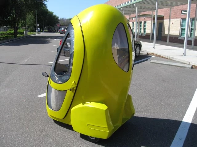 The three-wheeled electric vehicle is fitted with an electric hub motor in the front wheel, enclosed cab, tinted windows, a seat, and instrument display panel