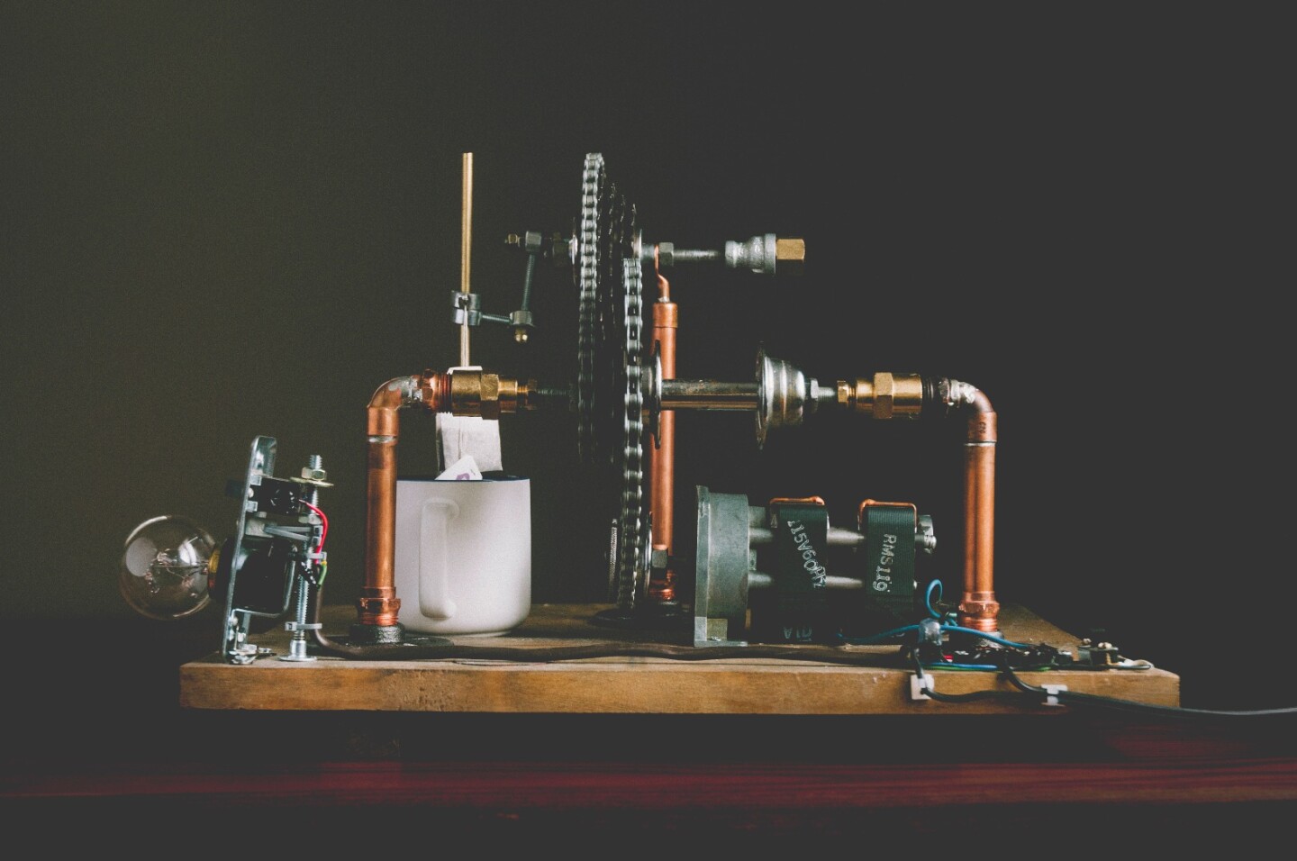 An electric motor turns a chained connected to a geared bike cassette, which spins a crank that dunks a teabag in a mug of hot water