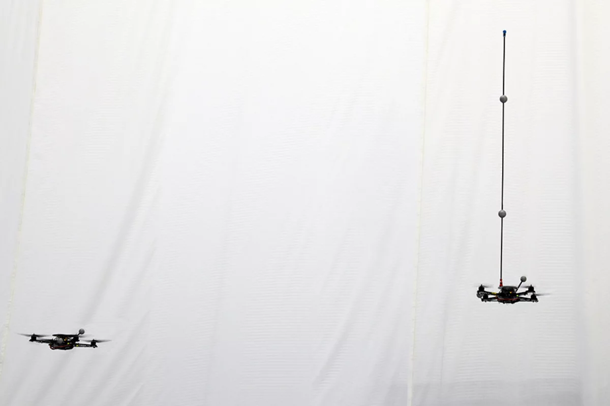 A quadrocopter robot balances a pole while a second robot waits to catch it