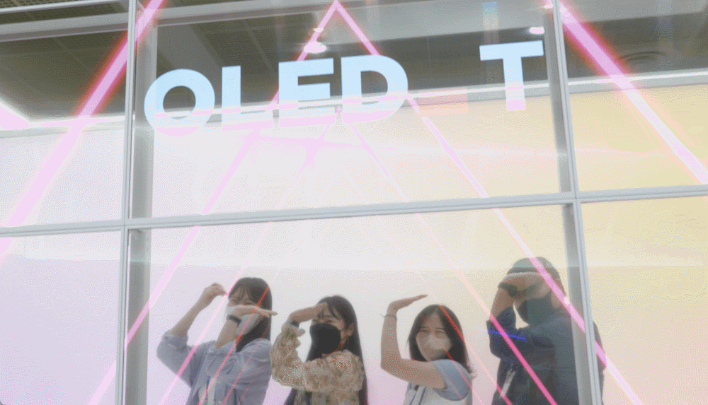 Trade show attendees doing their thing behind transparent OLED panels screening digital art or commercial videos