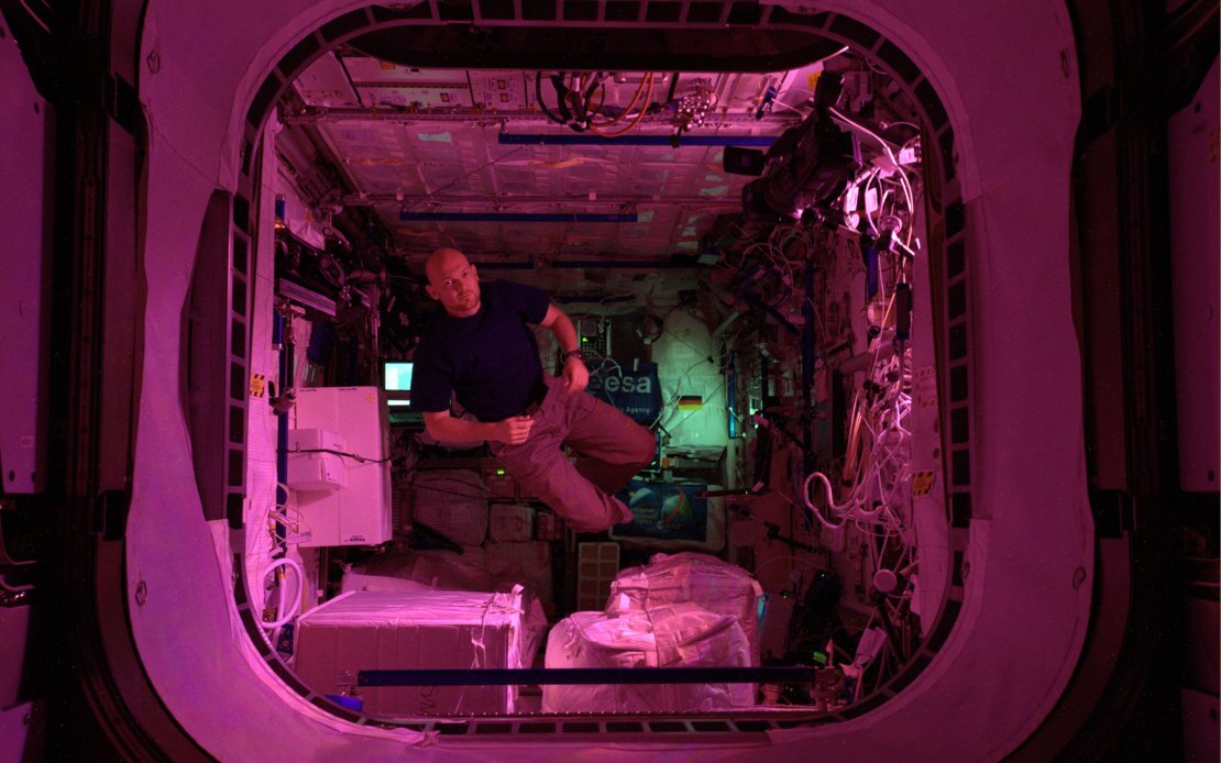 ESA astronaut Alexander Gerst floating weightless in the Columbus Laboratory – during the crew's off-duty time, the lighting in the module is dimmed to a pinkish glow