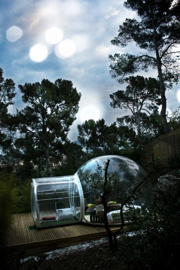 Each bubble is set up in a forested area on a flat, rigid floor near a wooden outhouse