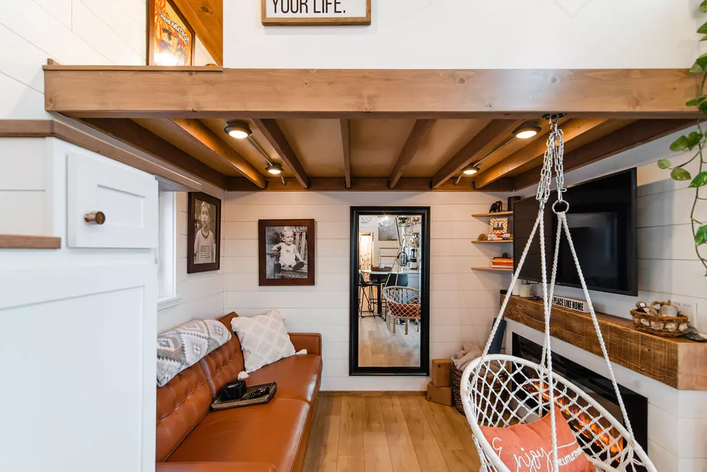 Jen's 34' x 10' Tiny Home includes a snug living room with a sofa and a TV, plus a neat suspended chair