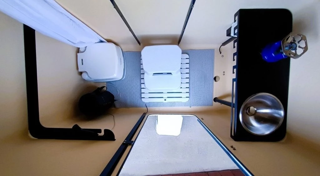 View from above at the Native's lower floor plan, which includes kitchen and bathroom shelving, a sink, a shower mat, a privacy curtain a floor-integrated drain, and a shower/faucet system – campers bring their own portable toilet, stove and gear