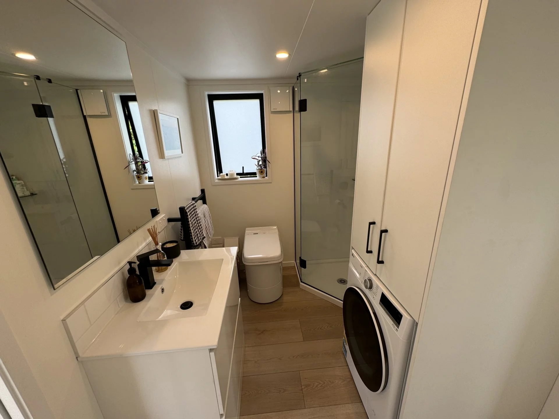 The bathroom in the Long Black (with loft) includes a vanity sink, shower, flushing toilet, and a washer/dryer