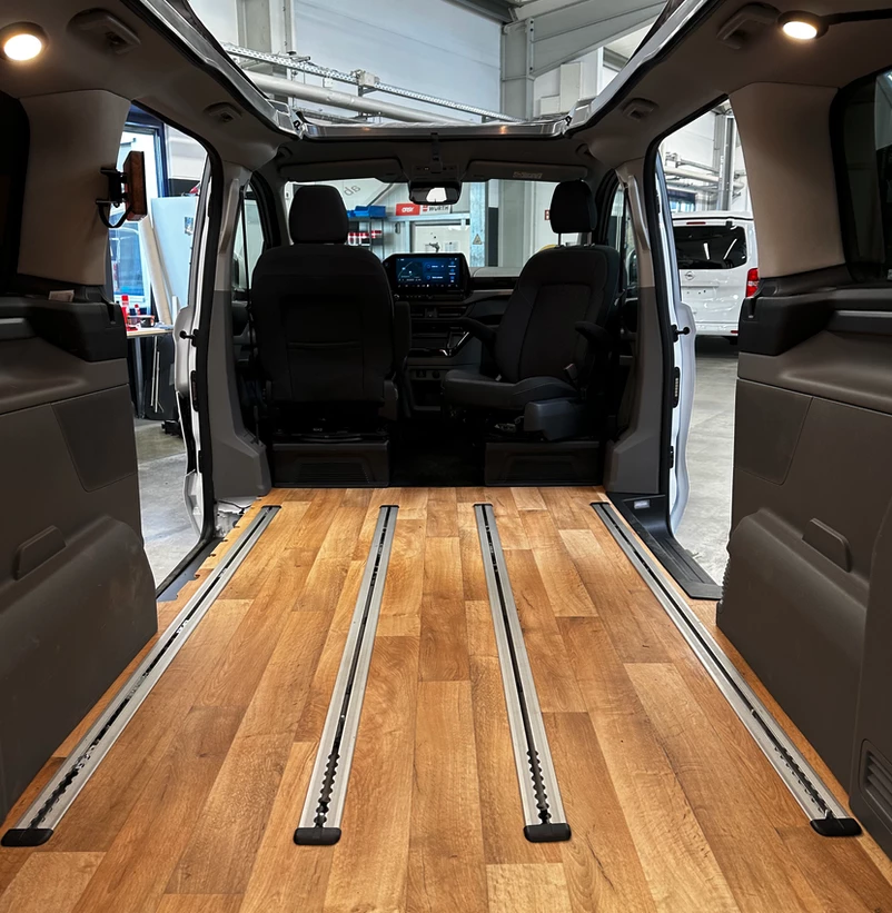 The added floor with airline-grade tracks is the key to the whole Vanexxt Ford conversion; also note the gooseneck lamps in the upper corners