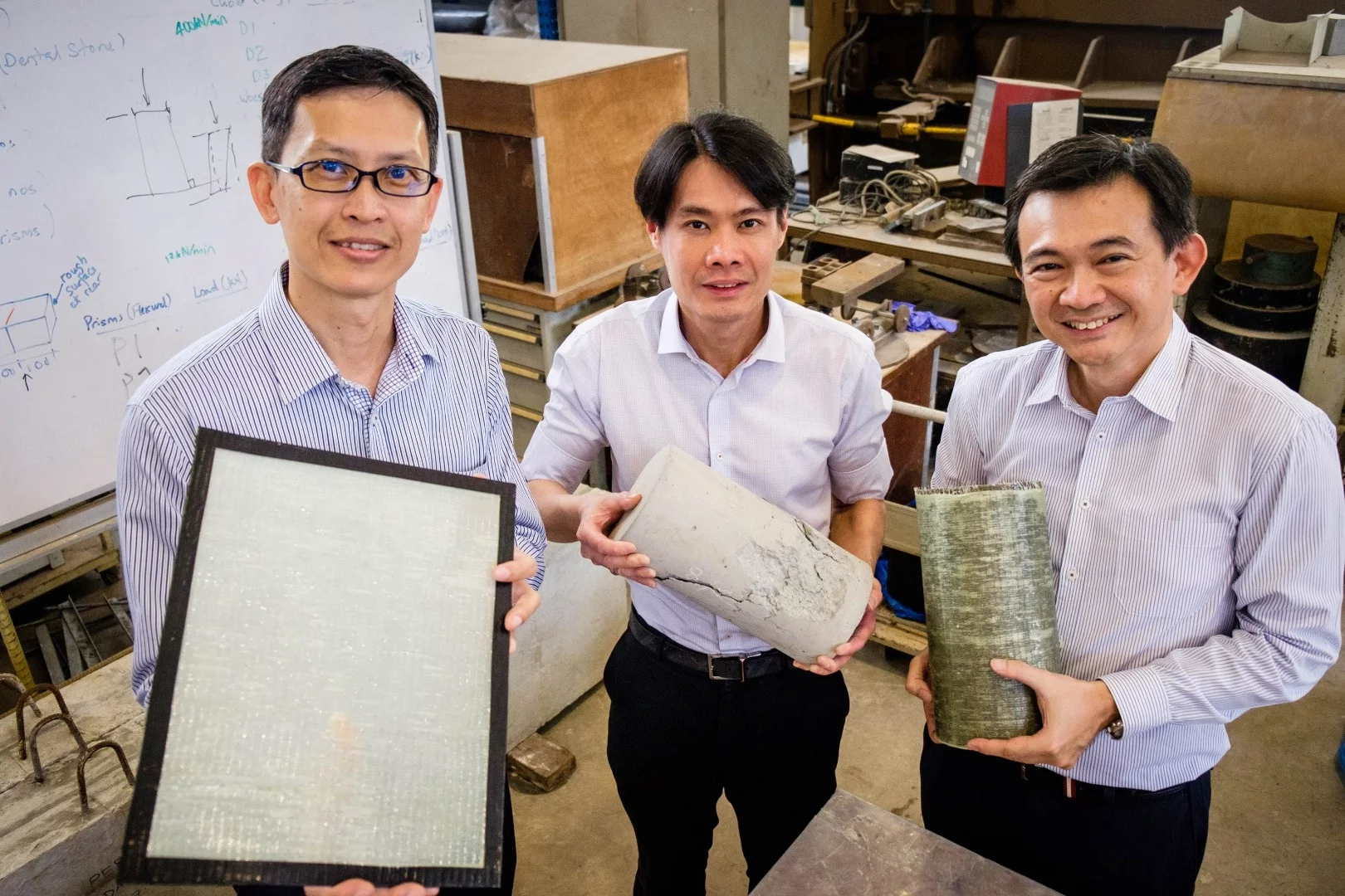 Assoc. Prof. Ng Kee Woei holding the FasRaP, JTC Group Director of Engineering Calvin Chung holding a concrete cylinder that was cracked under high pressure, and Prostruct Consulting Founder Dr. Ang Choon Keat holding a concrete cylinder reinforced with FasRaP
