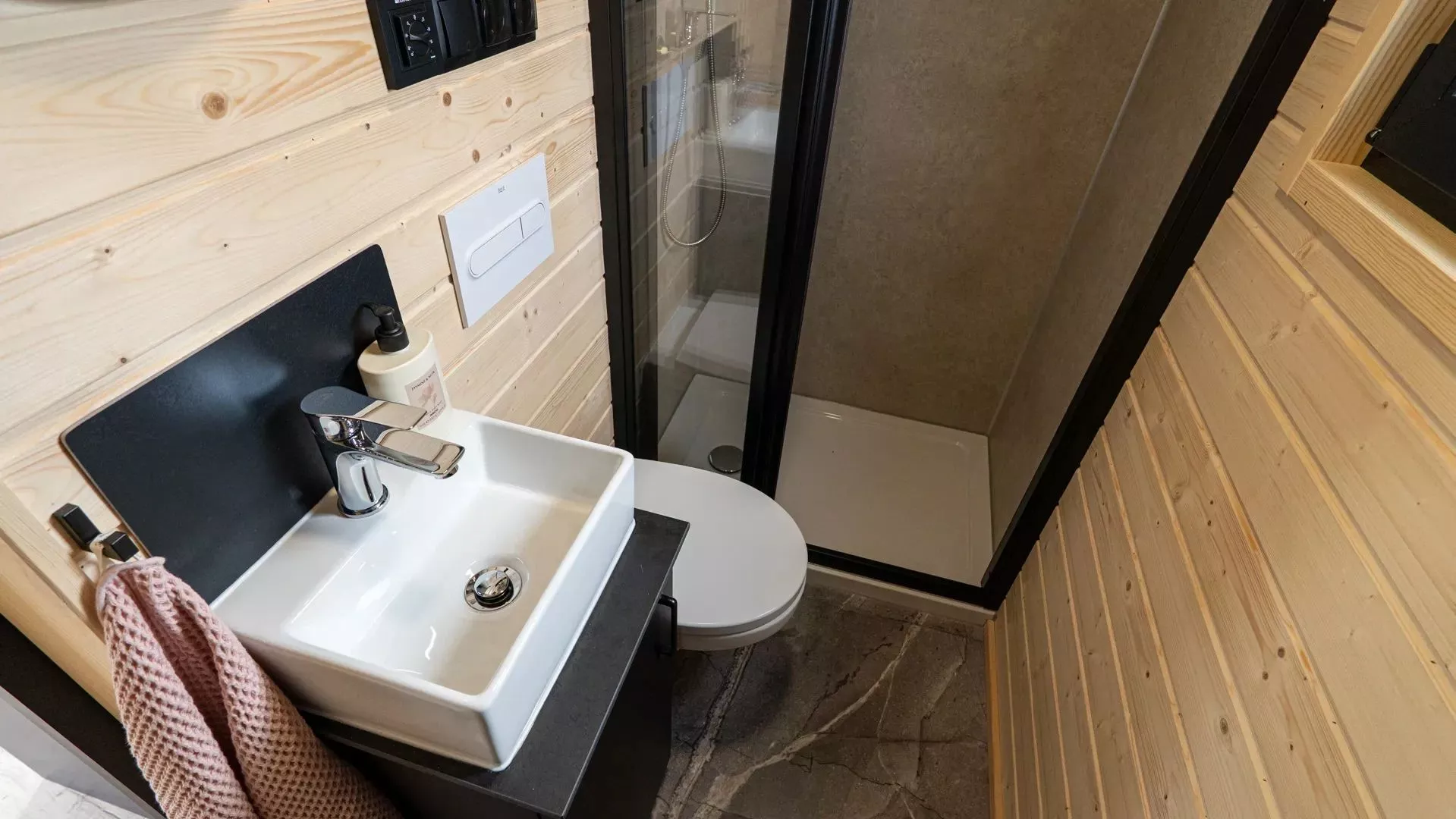 The Chocolate tiny house's relatively small bathroom features stone-like tile flooring, dark and light contrasts and a walk-in shower