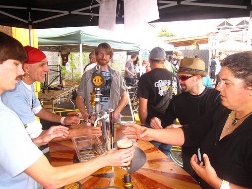 The Beer Bike is a custom-built cargo bicycle that features two beer kegs, a wooden bar with two serving taps, space for pizza boxes, and a solar-powered boom box