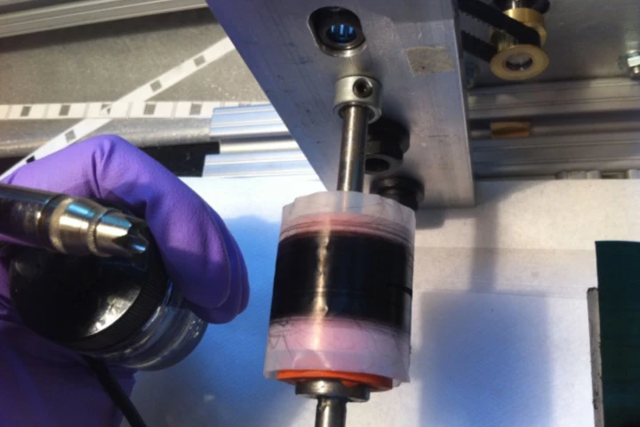 The ribbon-like material being wound onto a spool, while being sprayed with polymer and stretched