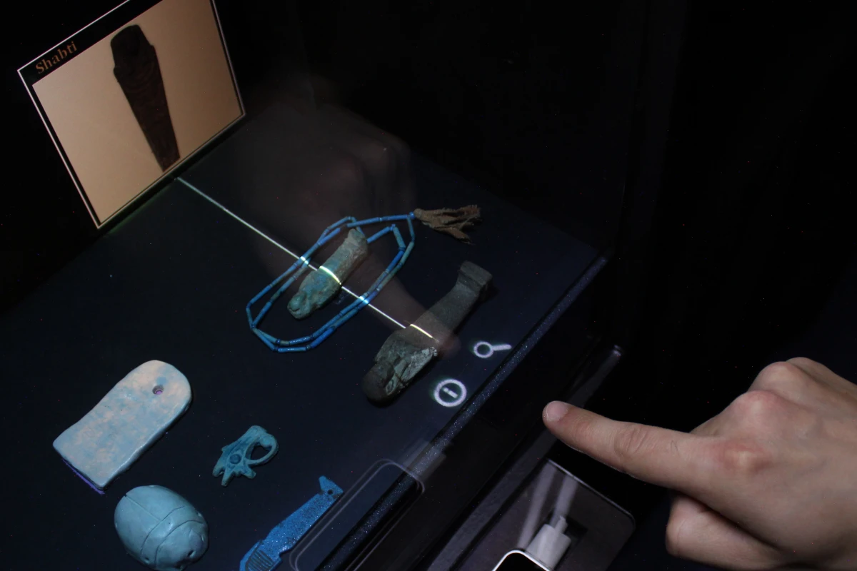 The reflection of a user's finger "touches" a museum artifact, causing a projected pop-up to appear