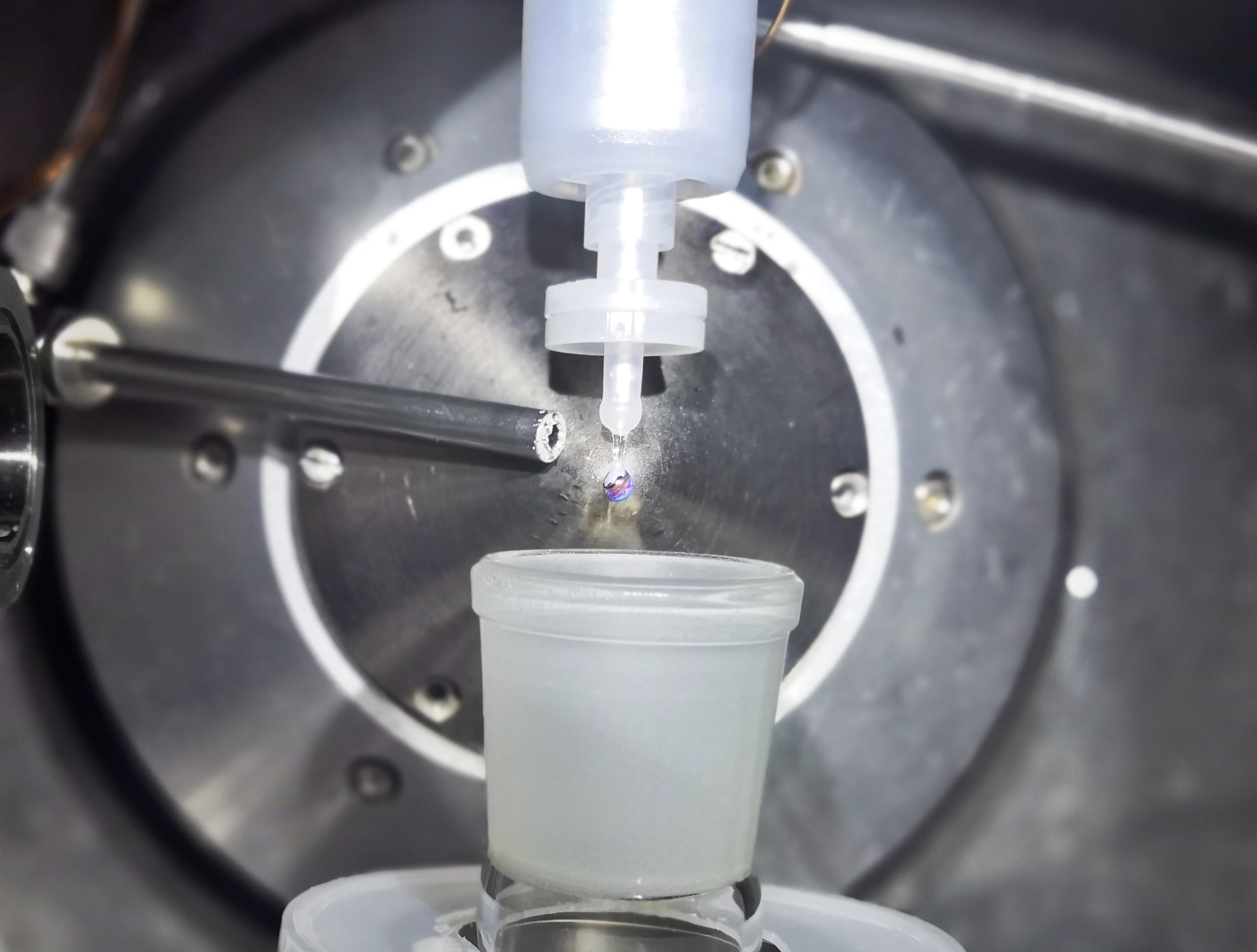 The experimental setup that produced the metallic water, including a nozzle that dripped sodium-potassium alloy and a tube that releases water vapor into the chamber