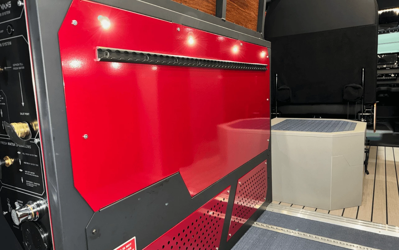 Water and plumbing equipment is stored in the driver-side wheel well console; also note the closed shower box with anti-slip top surface that works as a step up to the bed