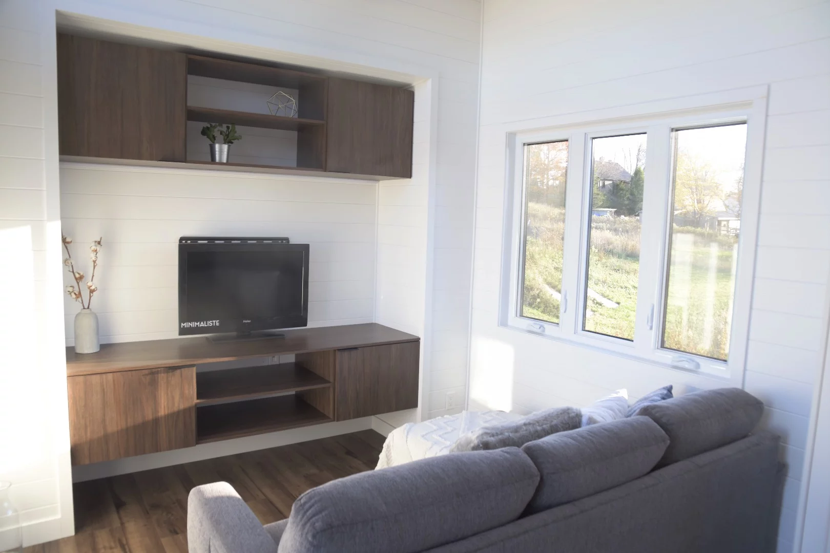 Visitors enter the Magnolia into an open living area with an entertainment center and some storage space, as well as a sofa