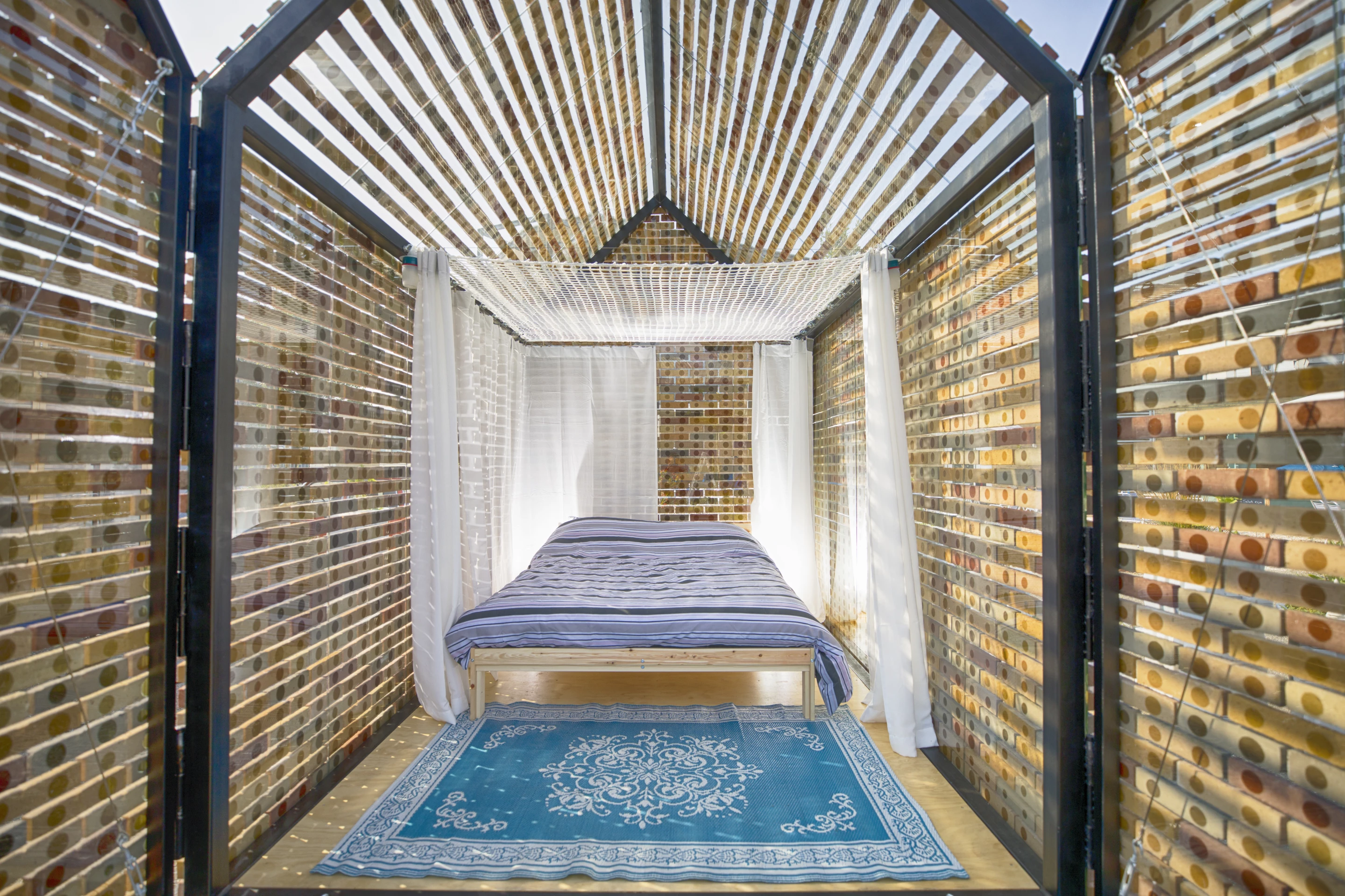 Floating Bricks is conceived as a habitable brick wall and consists of a simple glass shelter with a brick pattern on its exterior. It was designed by ROFFAA Architects