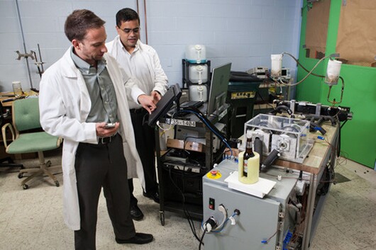 Michael Benedict (left) and Venkat Venkatakrishnan using GE’s magnetic refrigeration system to chill a bottle of Coors Light
