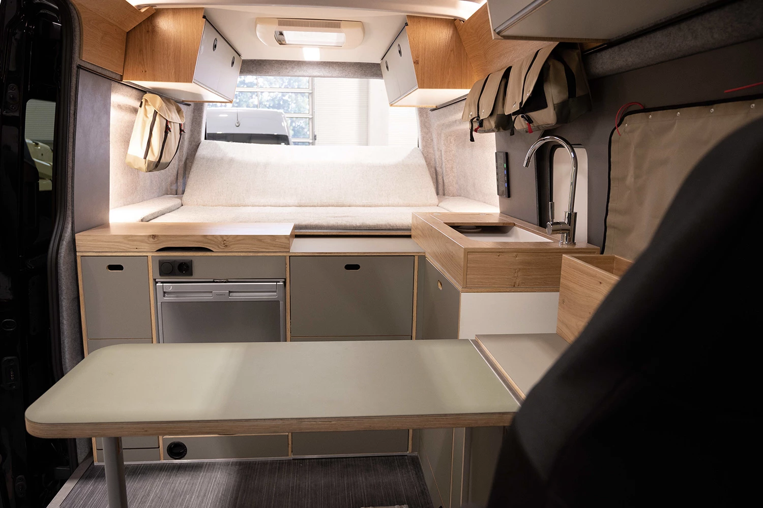The interior includes a detachable dining table, L-shaped kitchen, rear bed/lounge and swivel driver cab seats