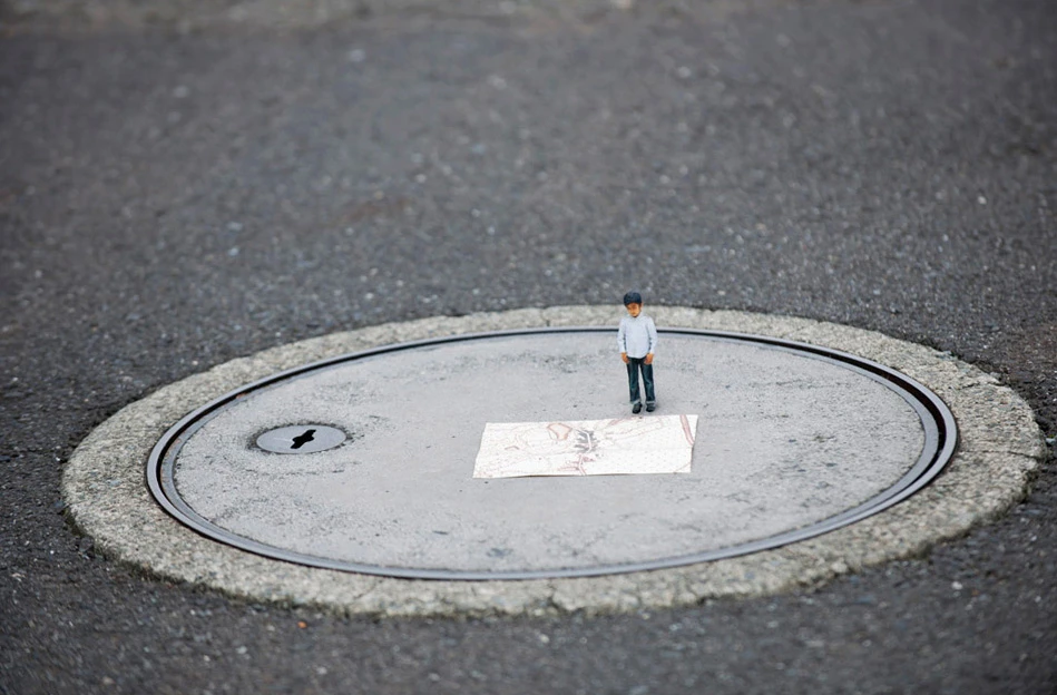 A 3D printed miniature of a child is dwarfed by a common manhole
