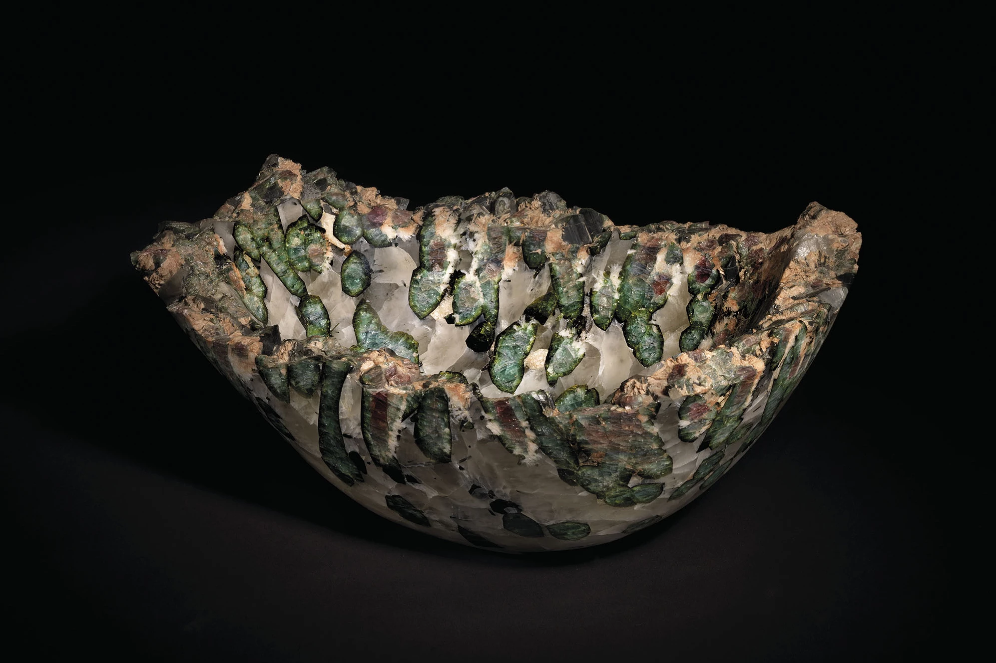 Originating in Brazil, this tourmaline bowl was created from a larger original specimen by polishing the interior and exterior to reveal cross-sections of large watermelon tourmaline crystals. The colours of the resultant 15 inch (38 cm) bowl range from black to purple, through greens and pinks, with the rim of the quartz matrix left in its original natural state.