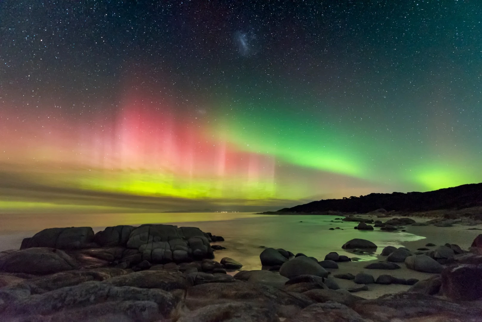 A brightly colored display of the Southern Lights beams high into the night sky on the east coast of Tasmania. The Large Magellanic Cloud also appears at the top centre of the image. Deserted beaches and minimal light pollution make Tasmania an ideal place to photograph the night sky, even more so when the aurora comes out to play. St Helens, Tasmania, Australia, 20 April 2018