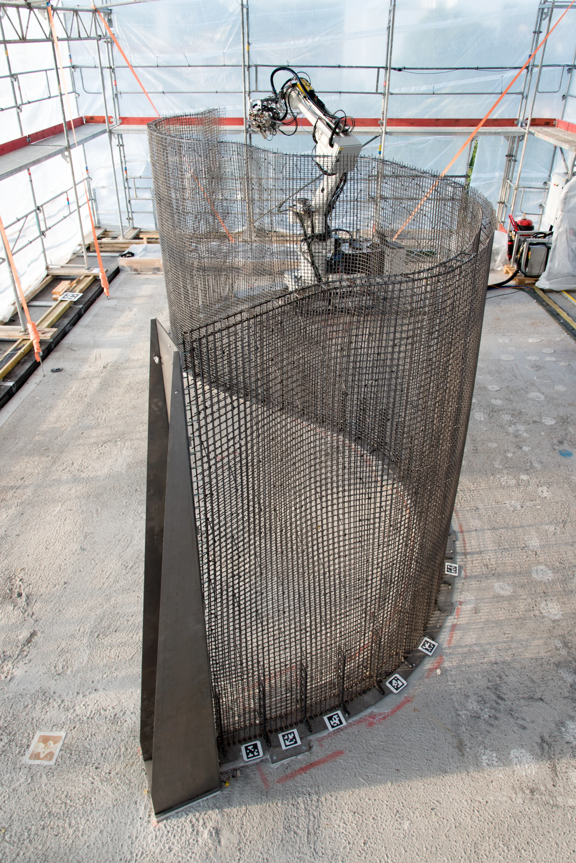 The robot moves autonomously along on caterpillar tracks, using the toolhead to bend and weld 6 mm steel rebar to construct the mesh wall framework