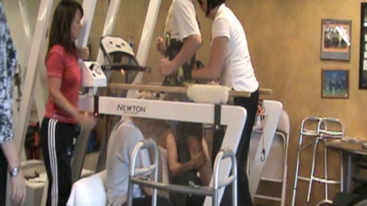 A team of physio staff helping Godfrey to move his legs on a treadmill