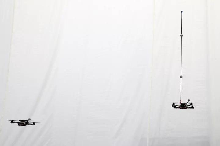 A quadrocopter robot balances a pole while a second robot waits to catch it