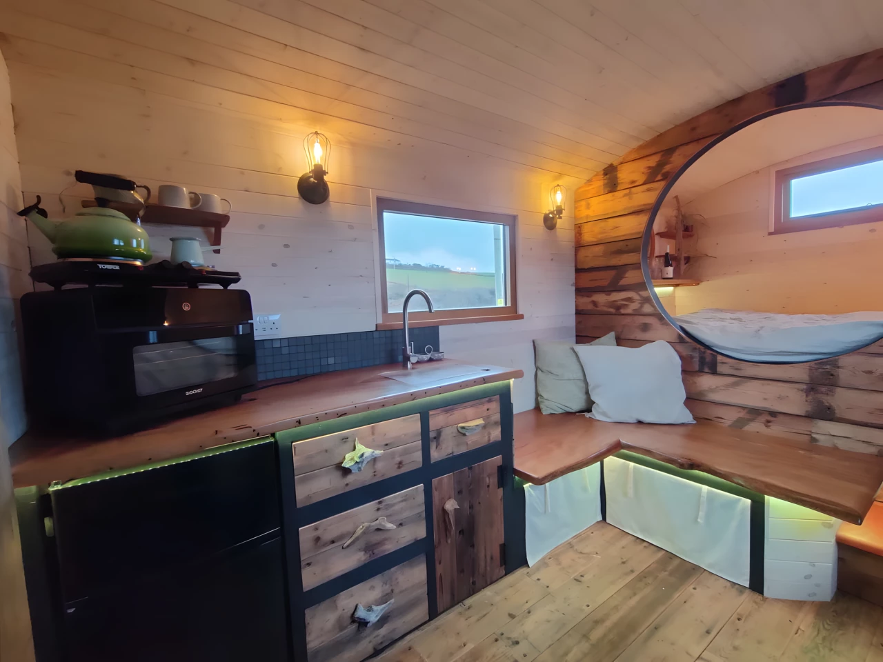 Double doors open onto the tiny house's living room, which includes an L-shaped seating area with integrated storage