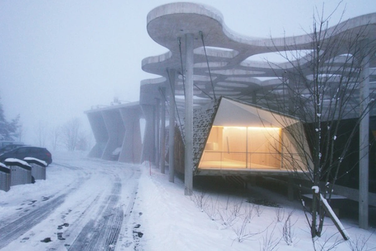 The "Suspended Forest" cabin hangs from a large overhead concrete structure, allowing the dwelling to hover above the snow-covered landscape