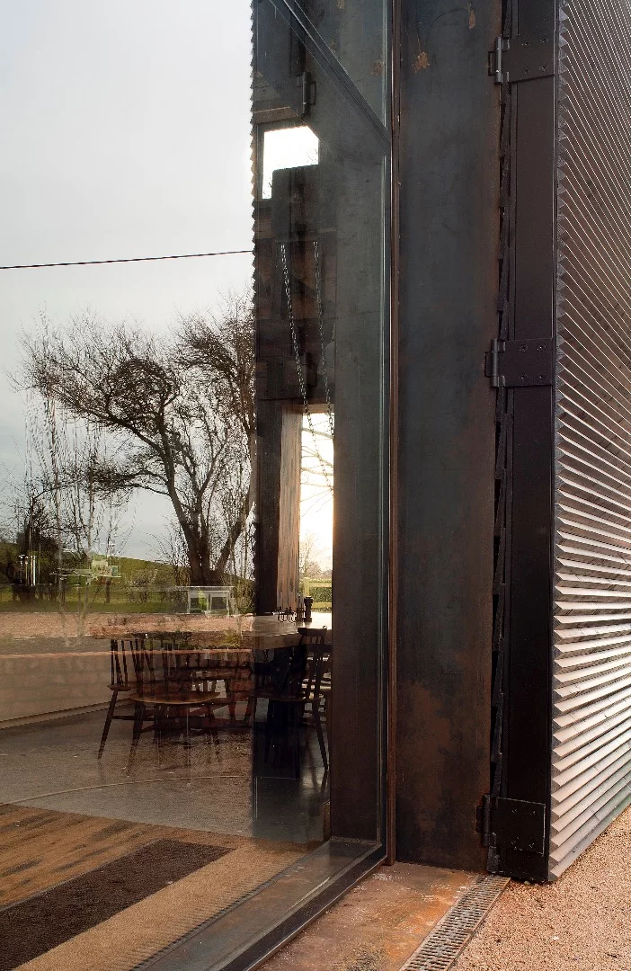 This glazed area (pictured) can be lifted by manipulating an industrial mechanism adapted from a chain lift, thus opening the interior of the home to the outside