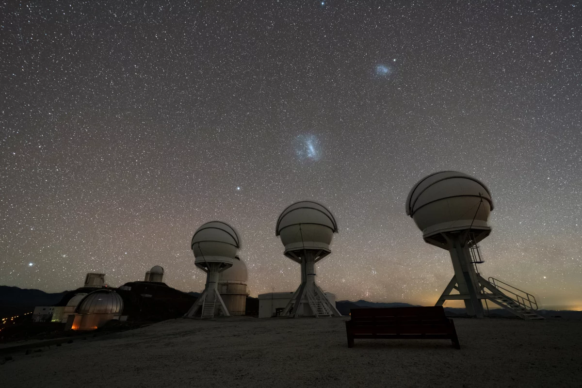 Shown in this nighttime image are the three telescopes of the BlackGEM array at ESO’s La Silla Observatory in Chile. The Large and Small Magellanic Clouds can be seen just above the telescopes. The BlackGEM array can quickly scan large areas of the sky to find a source that has emitted gravitational waves detected by LIGO and Virgo.
