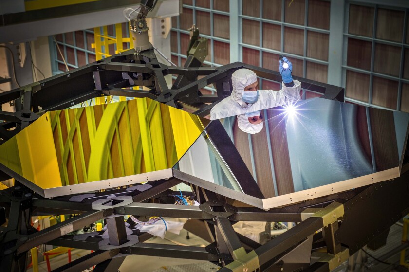 JWST Optical Engineer Larkin Carey examines two test mirror segments recently placed on a black composite structure (Photo: NASA/Chris Gunn)