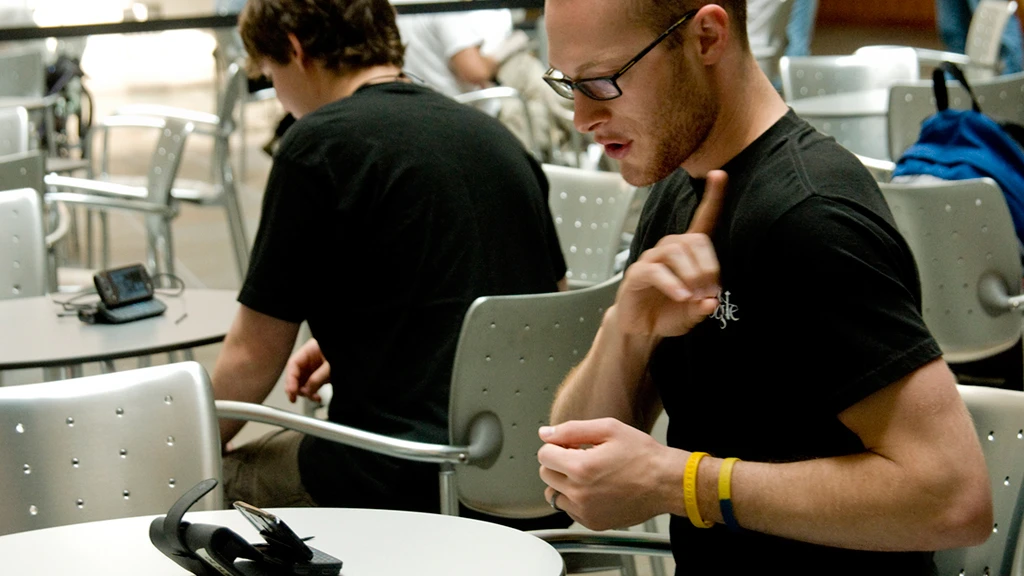 Josiah Cheslik, a UW junior and volunteer in the MobileASL field study, demonstrates using the phone to sign with Pete Michor, seen in the background, another participant in the study (Image: Mary Levin, UW)