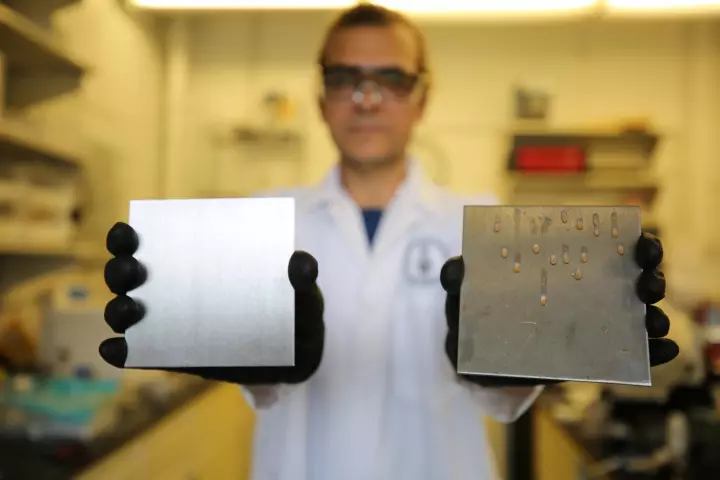 Dr. Tarek Awad shows two samples: at left, a stainless steel surface treated to trap simple cooking oil, and at right, an uncoated surface