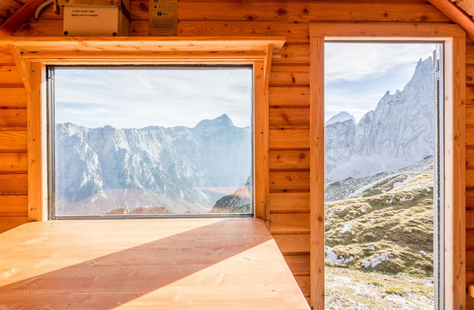 Furniture inside Bivak II na Jezerih includes a folding table, a bench, and sleeping area