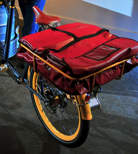 The Beer Bike is a custom-built cargo bicycle that features two beer kegs, a wooden bar with two serving taps, space for pizza boxes, and a solar-powered boom box