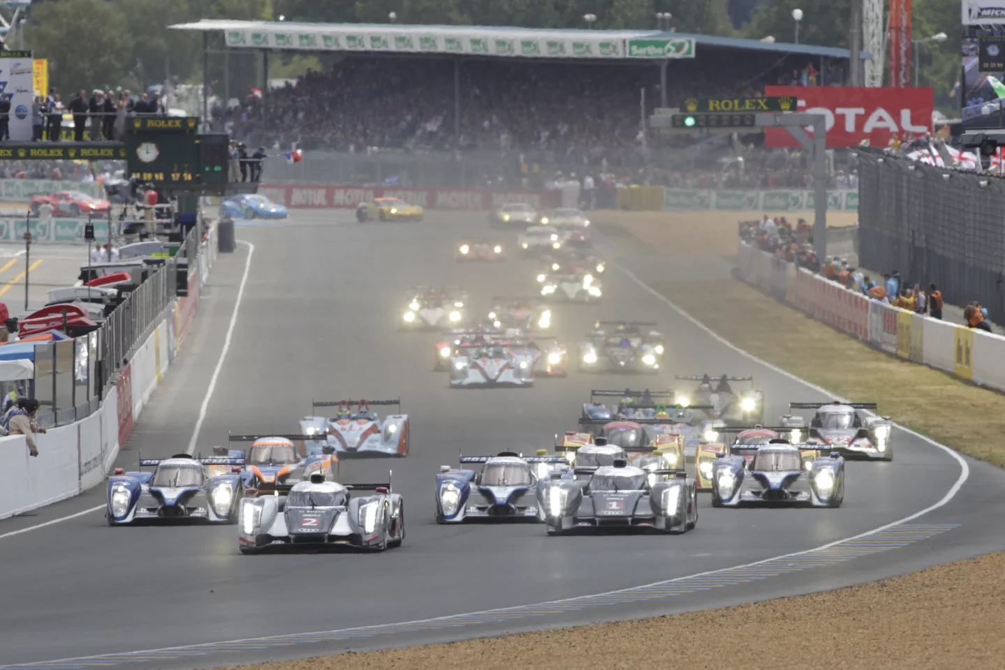 The beginning of the 2011 Le Mans 24 hour and two Audis narrowly lead a gaggle of Peugeots
