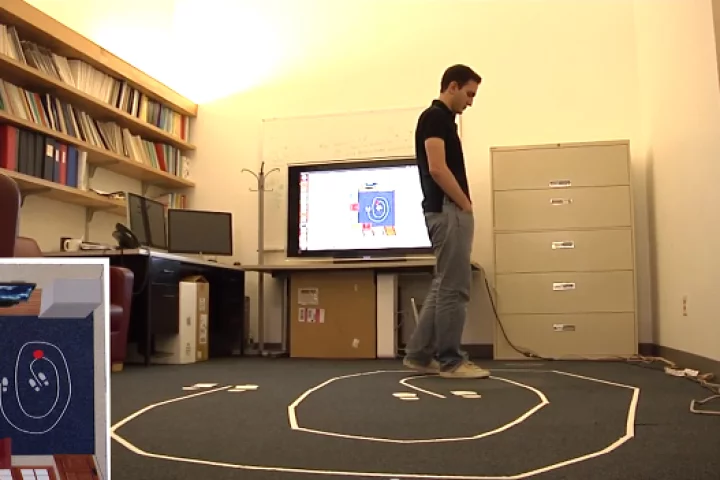 A subject's position is tracked by a WiTrack system (screen at lower left) located in another room