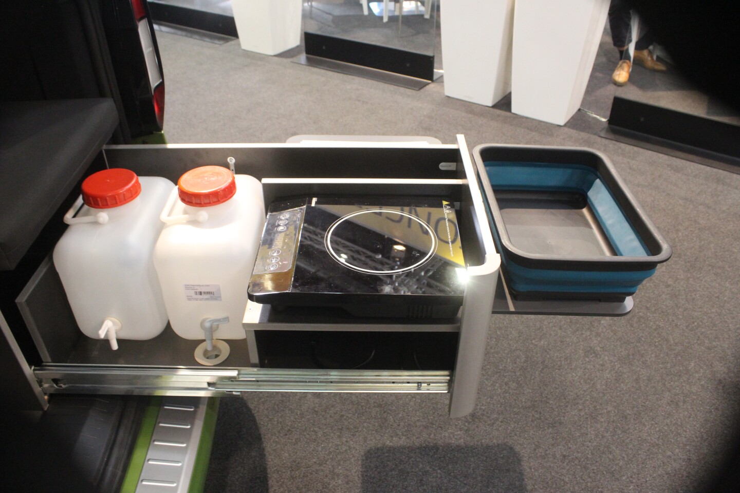 The simple slide-out kitchen has dual water canisters with spouts, a cooker, and an attachable extension to hold the collapsible sink basin