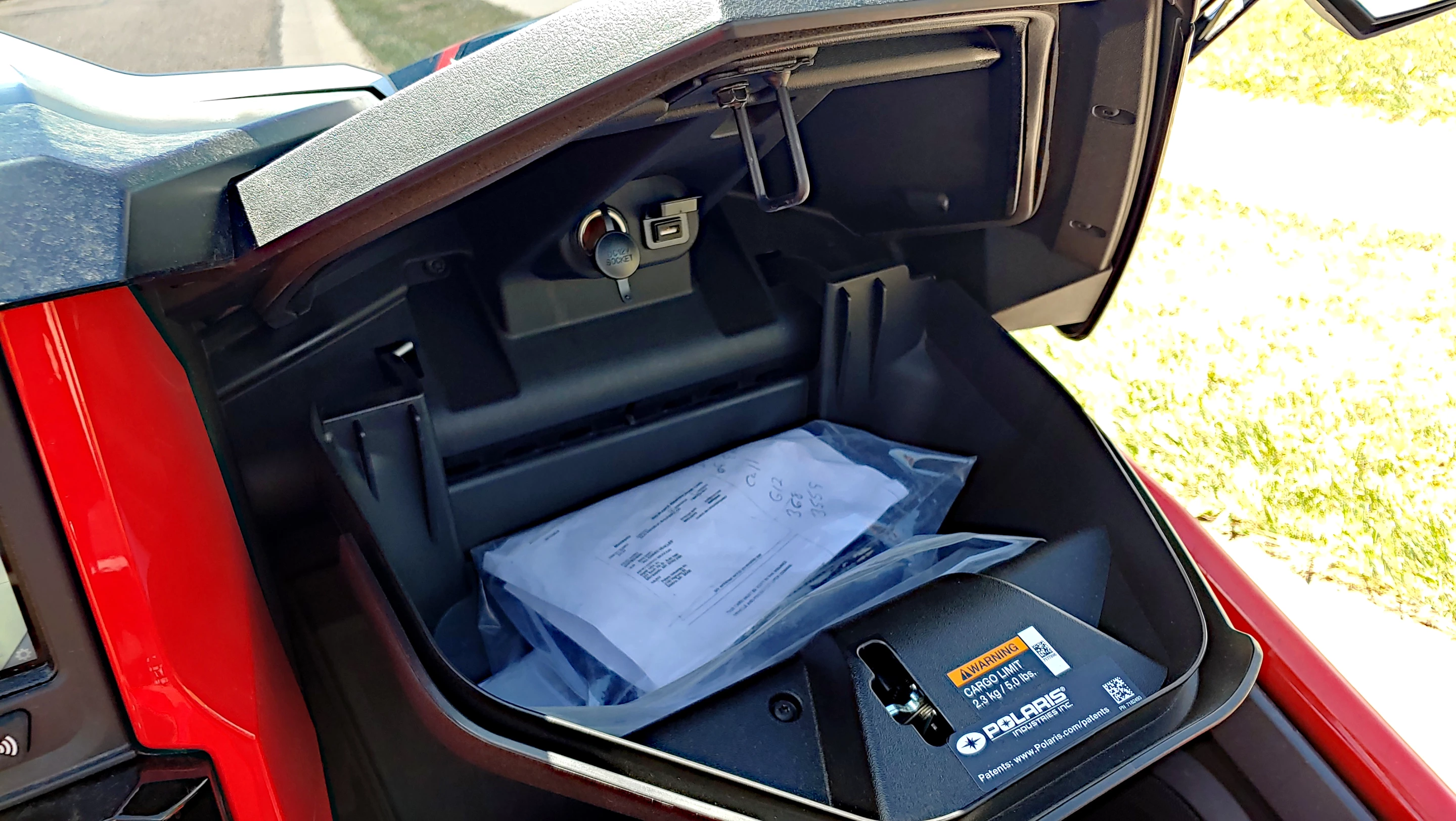 Although it closes well up and out of the way of the passenger's knees, the Slingshot's large clamshell glove box has a lot of storage space plus plugs