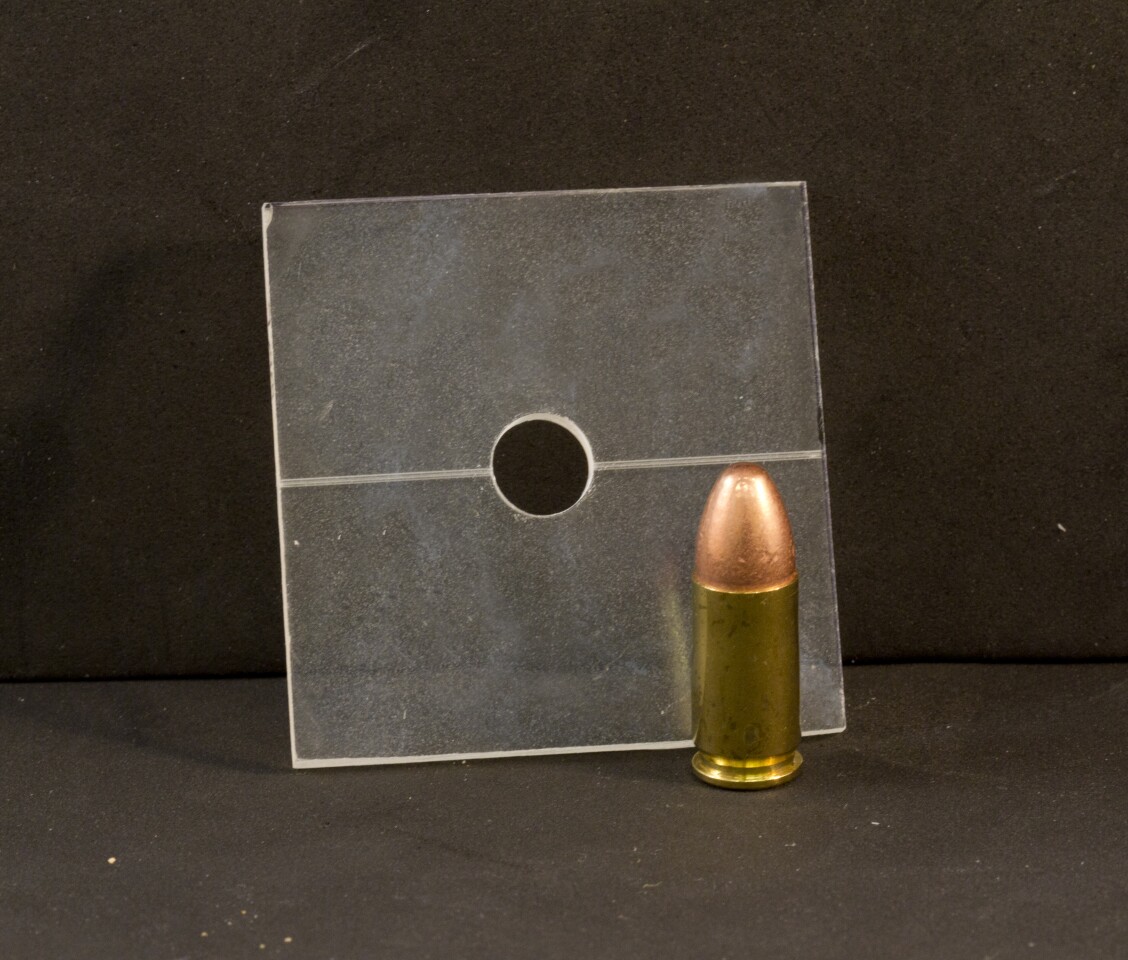 A 9 mm hole in a sheet of plastic next to a 9 mm cartridge