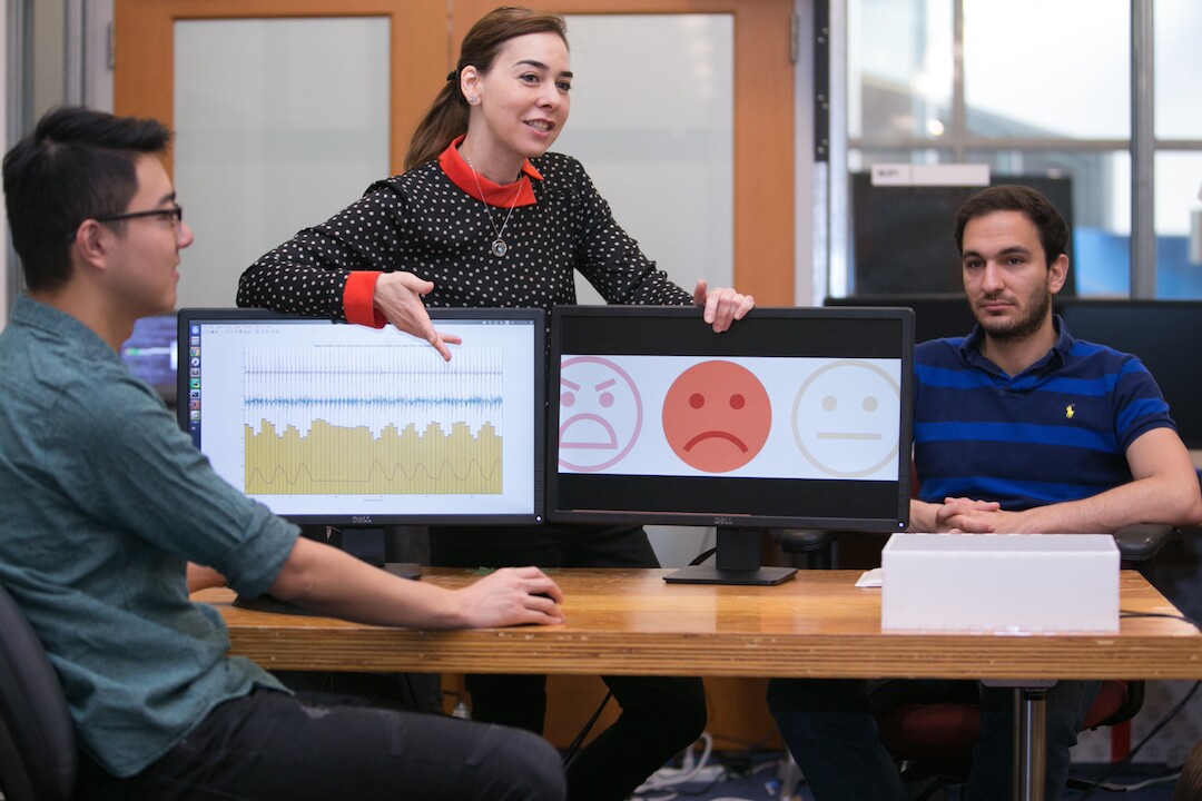 Dina Katabi (center) demonstrates that although Fadel Adib's face (right) is neutral, the system can read his breathing and heart rate and determine that he is feeling sad