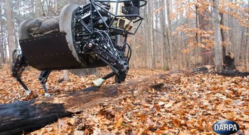 Boston Dynamics' quadruped steps over a log as it follows a soldier a few meters ahead of it