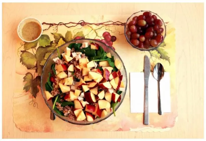 This image shows one of the study's unprocessed lunches, consisting of a spinach salad with chicken breast, apple slices, bulgur, and sunflower seeds and grapes