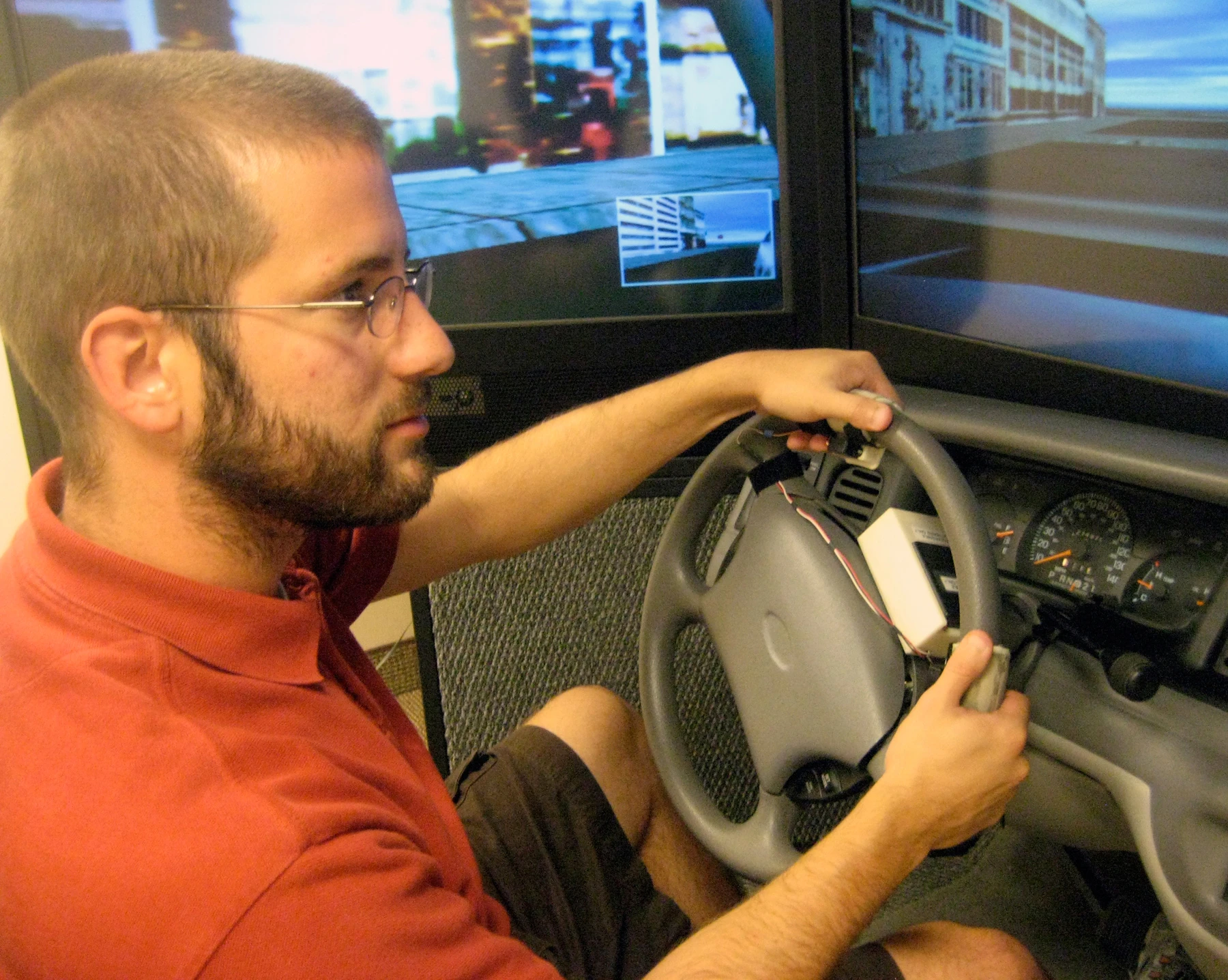 University of Utah psychology doctoral student, Nate Medeiros-Ward, operates a driving simulator with a steering wheel equipped with two touch devices that pull the skin on his index fingertips left or right (Image: Justin Lukas, University of Utah)