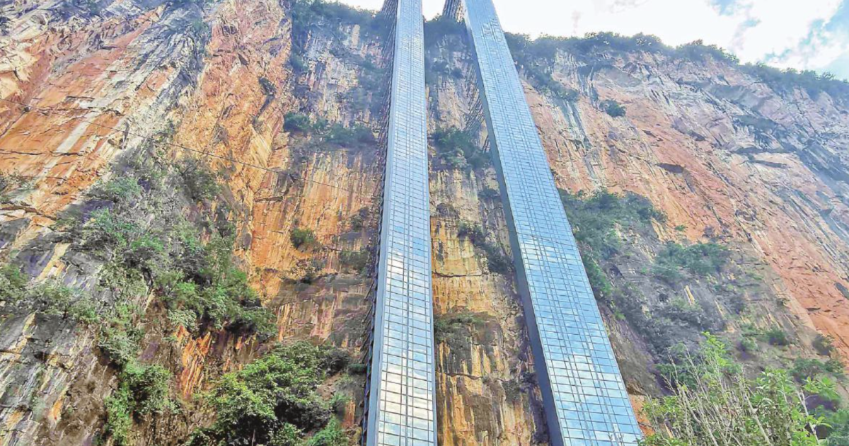 A glass-walled elevator ascending a steep canyon cliff face in a mountainous landscape.